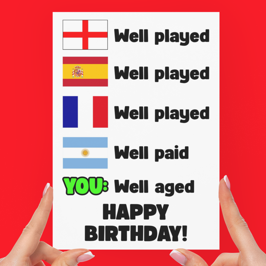 A white greeting card held up by two hands against a solid red background. The card features rows of national flags with the text 'Well played' and 'Well paid', with the final line highlighted in green and black as 'YOU: Well aged HAPPY BIRTHDAY!'.