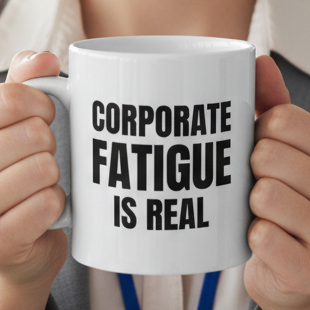 A woman in a gray blazer holds a white ceramic mug with the text 'CORPORATE FATIGUE IS REAL' printed in black. The background shows a softly blurred modern office interior with windows, desks, and a plant.