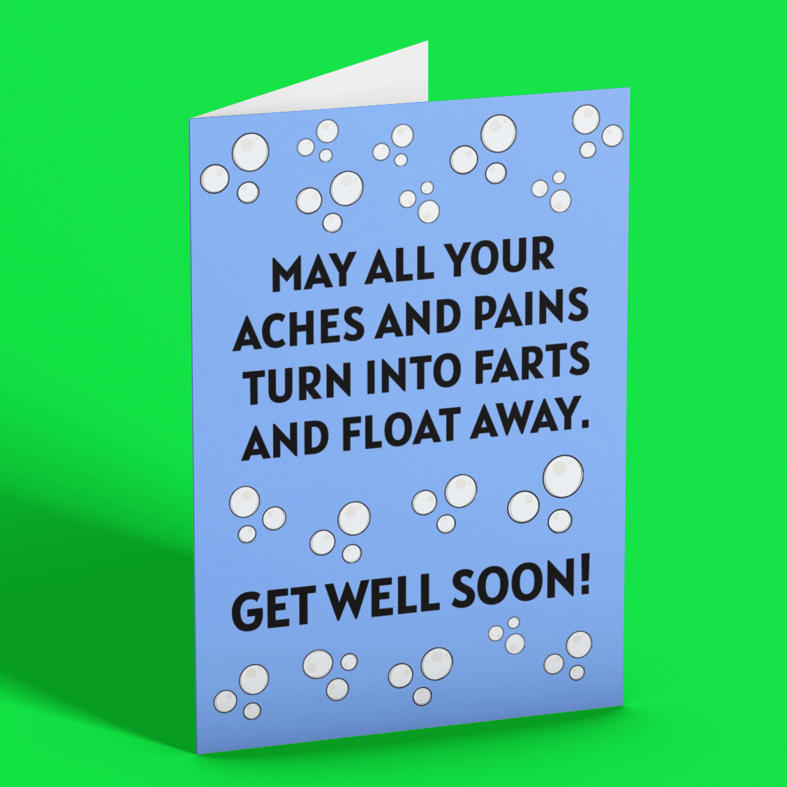 A folded greeting card with a light blue background and white bubble graphics, standing upright on a bright green background. The card features black text that reads, 'MAY ALL YOUR ACHES AND PAINS TURN INTO FARTS AND FLOAT AWAY.