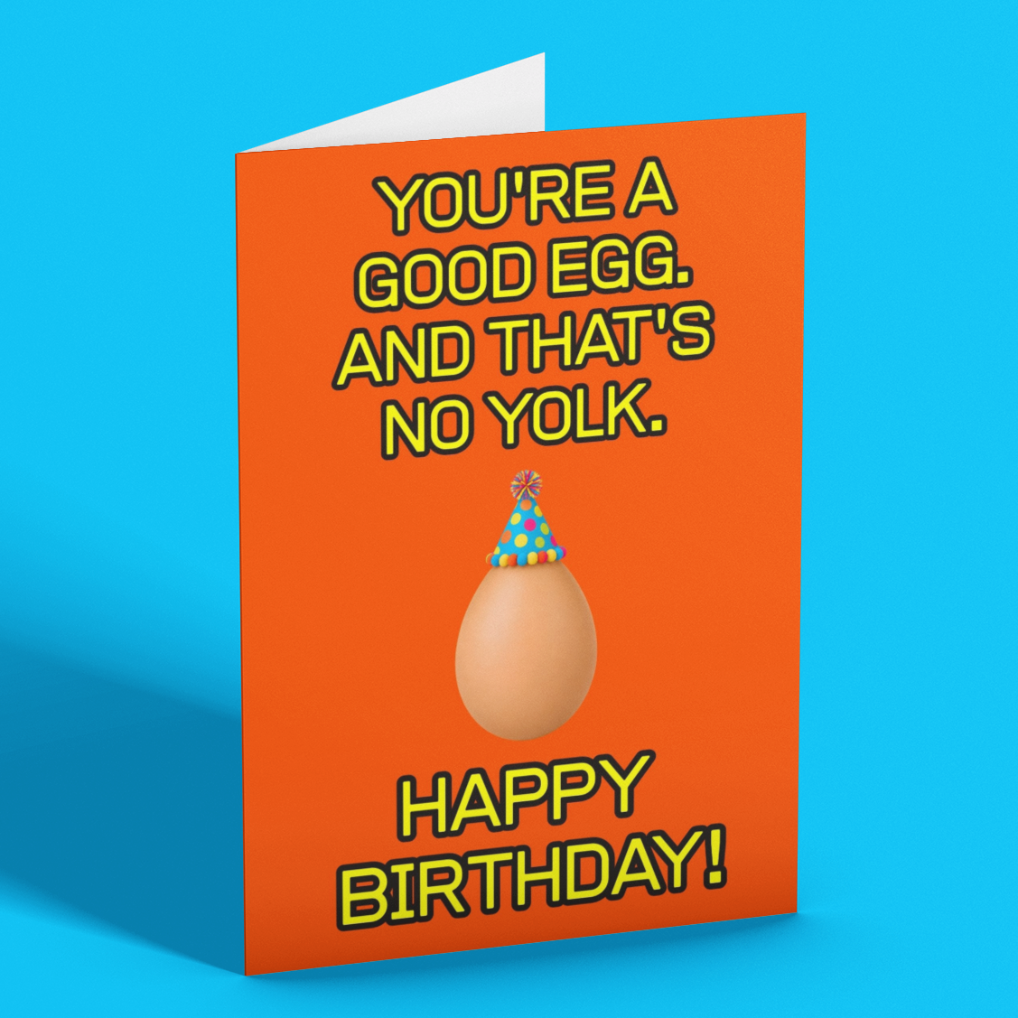A folded greeting card standing upright on a bright blue background. The card is orange with yellow text reading 'YOU'RE A GOOD EGG.