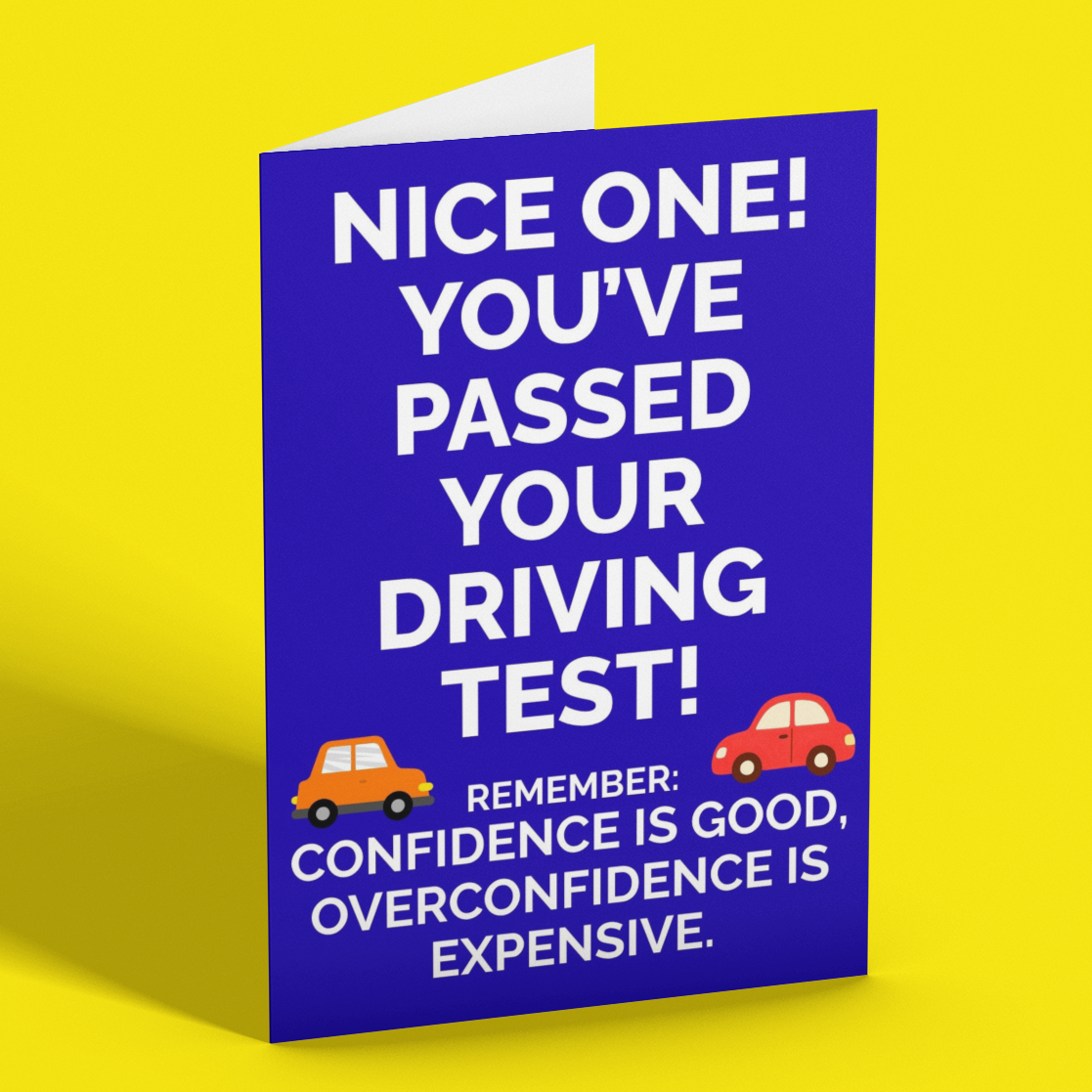 A blue greeting card with white text that reads 'NICE ONE! YOU'VE PASSED YOUR DRIVING TEST!' and a humorous driving test warning, shown standing on a bright yellow background.