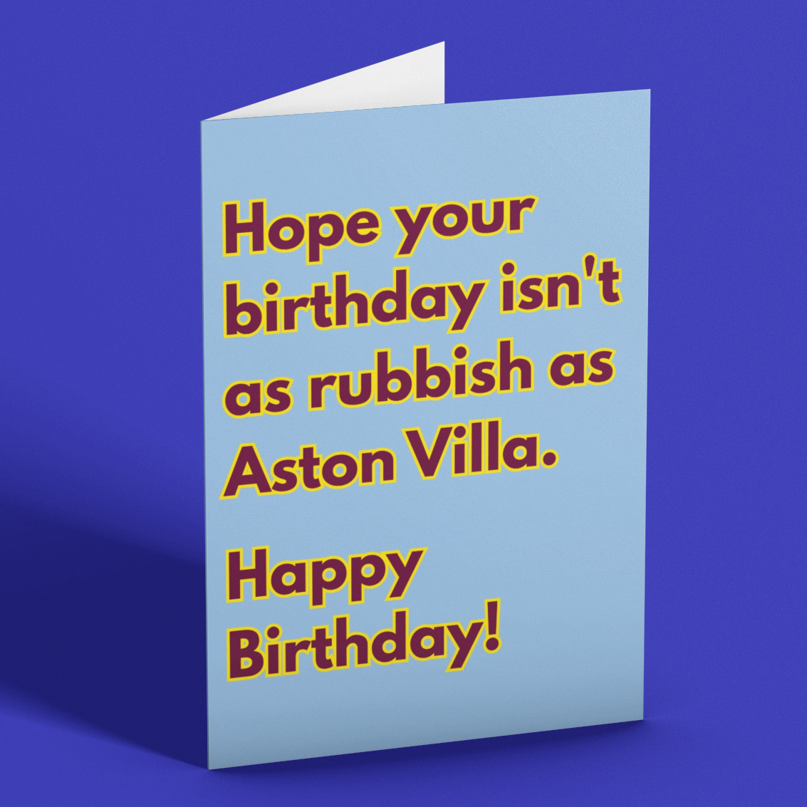 A folded greeting card standing upright on a solid blue background. The card is light blue with bold brown text that reads, 'Hope your birthday isn't as rubbish as Aston Villa.