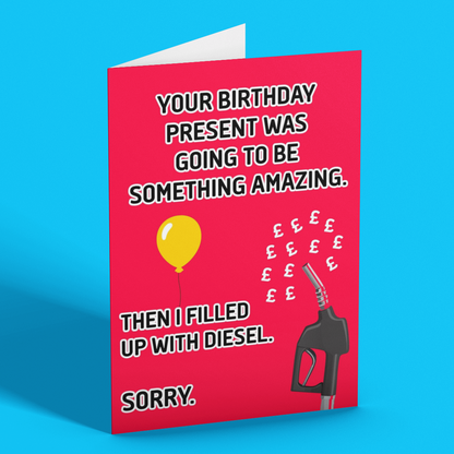 A folded greeting card standing upright on a bright blue background. The card is bright pink with white and black text that reads, 'YOUR BIRTHDAY PRESENT WAS GOING TO BE SOMETHING AMAZING.