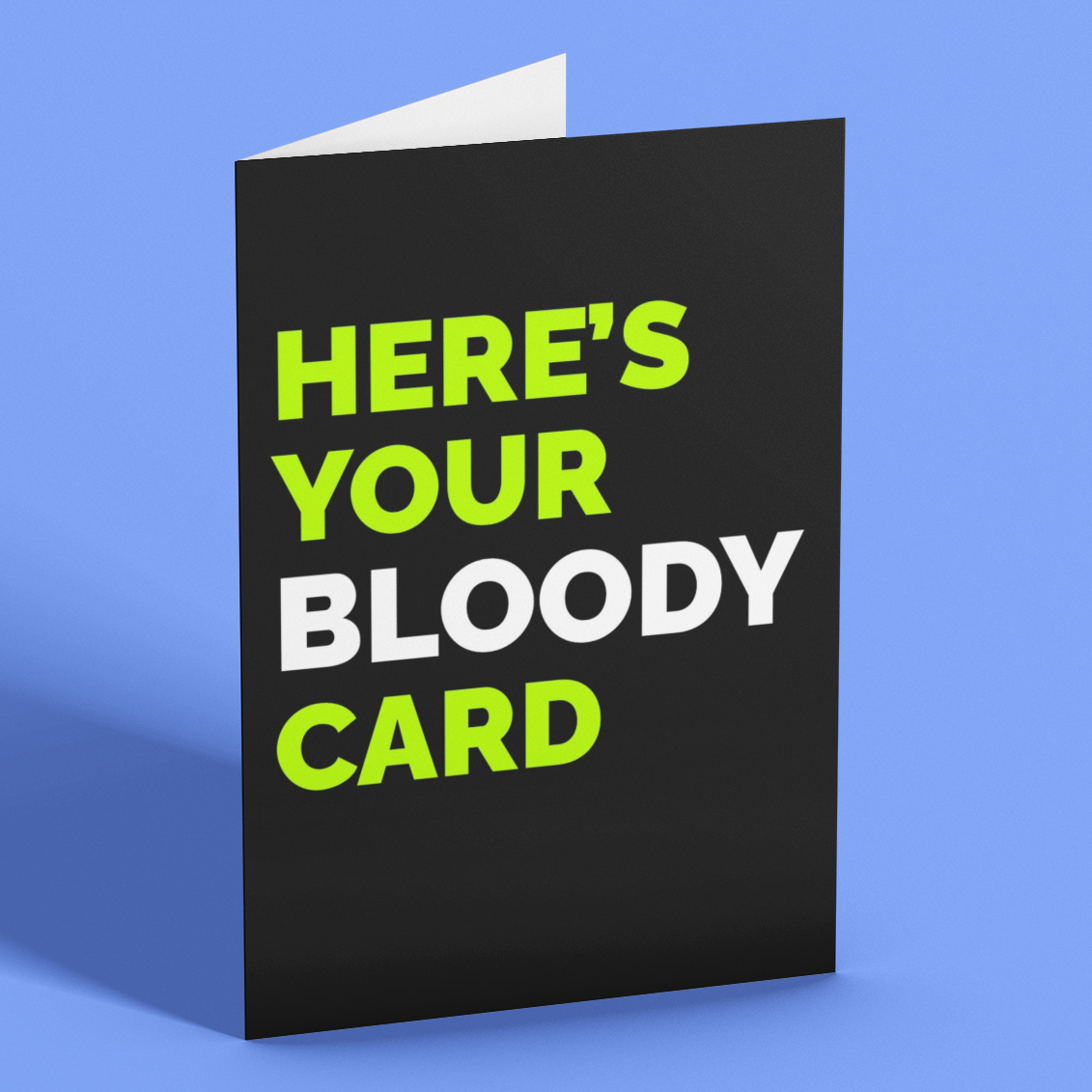 A folded greeting card standing upright on a blue background. The card has a black front with the text 'HERE'S YOUR BLOODY CARD' in bright neon green and white, with a white interior fold visible at the top.