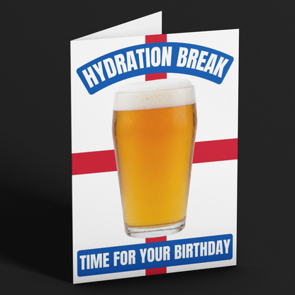 A folded greeting card standing upright on a dark gray background. The card features a white base with a red cross motif, a large photo of a frothy beer glass in the center, and blue text reading 'HYDRATION BREAK' at the top and 'TIME FOR YOUR BIRTHDAY' at the bottom.