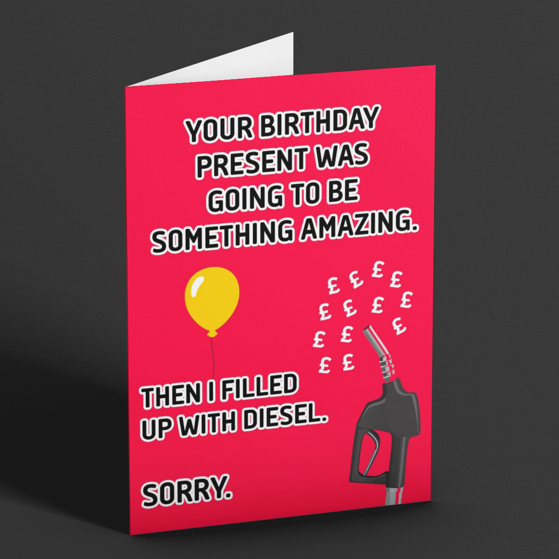 A folded greeting card standing upright on a dark gray background. The card has a bright red front with white text that reads, 'YOUR BIRTHDAY PRESENT WAS GOING TO BE SOMETHING AMAZING.