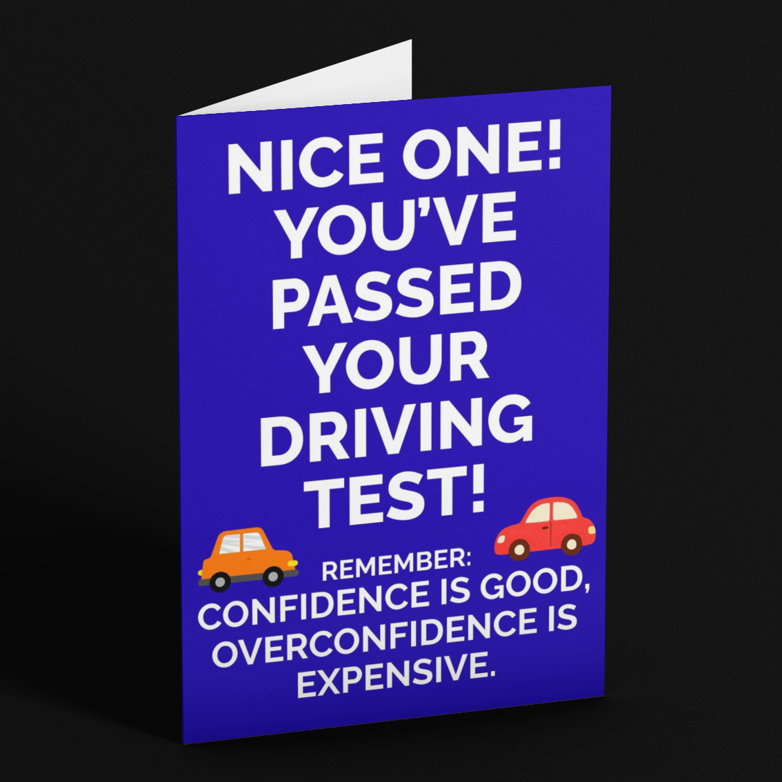 A folded blue greeting card standing upright on a black background. The card has white text that reads 'NICE ONE! YOU'VE PASSED YOUR DRIVING TEST!' with small cartoon car illustrations and additional text below.