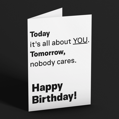A folded white greeting card standing upright on a dark gray background. The card has black text that reads, 'Today it's all about YOU.