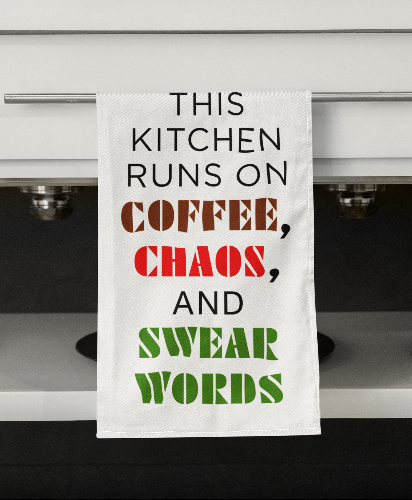 Kitchen towel with humorous text hanging on a kitchen cabinet.