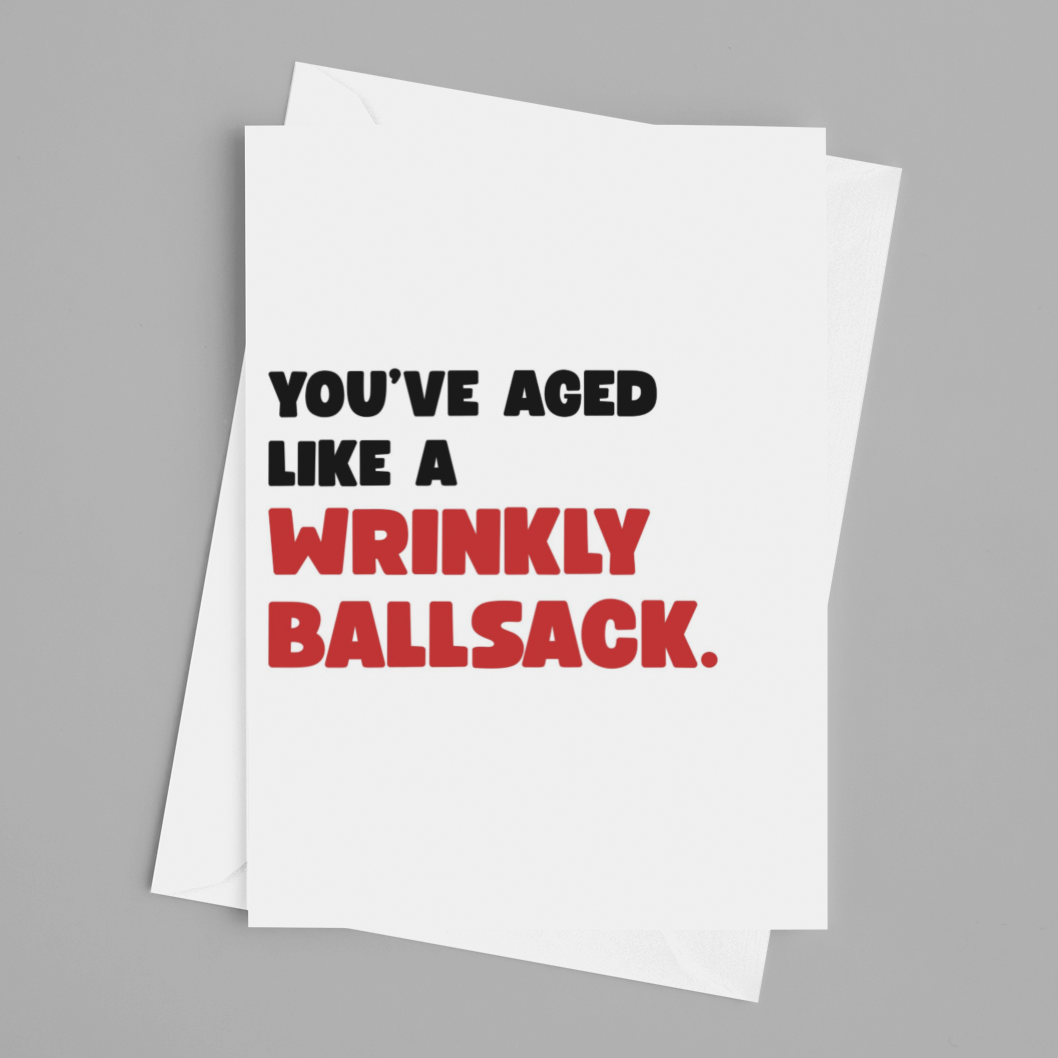 A white greeting card with humorous text reading 'YOU'VE AGED LIKE A WRINKLY BALLSACK.' in black and red lettering, shown on a neutral gray background.