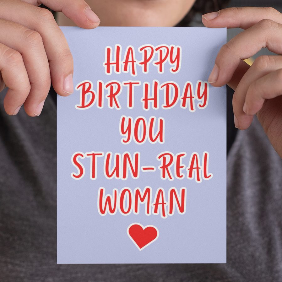 Person holding a card with 'Happy Birthday you STUN-REAL WOMAN' text and a heart symbol.