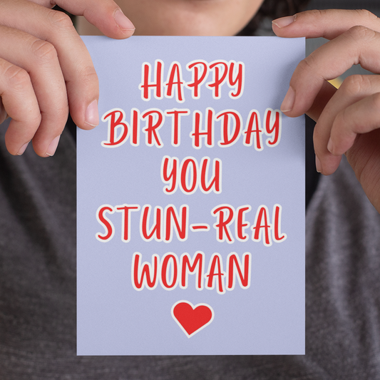 Person holding a card with 'Happy Birthday you STUN-REAL WOMAN' text and a heart symbol.