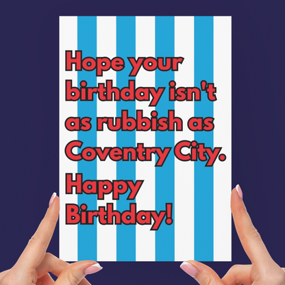 A person holds a square birthday card with blue and white vertical stripes and red text that reads, 'Hope your birthday isn't as rubbish as Coventry City. Happy Birthday!' against a dark navy background.