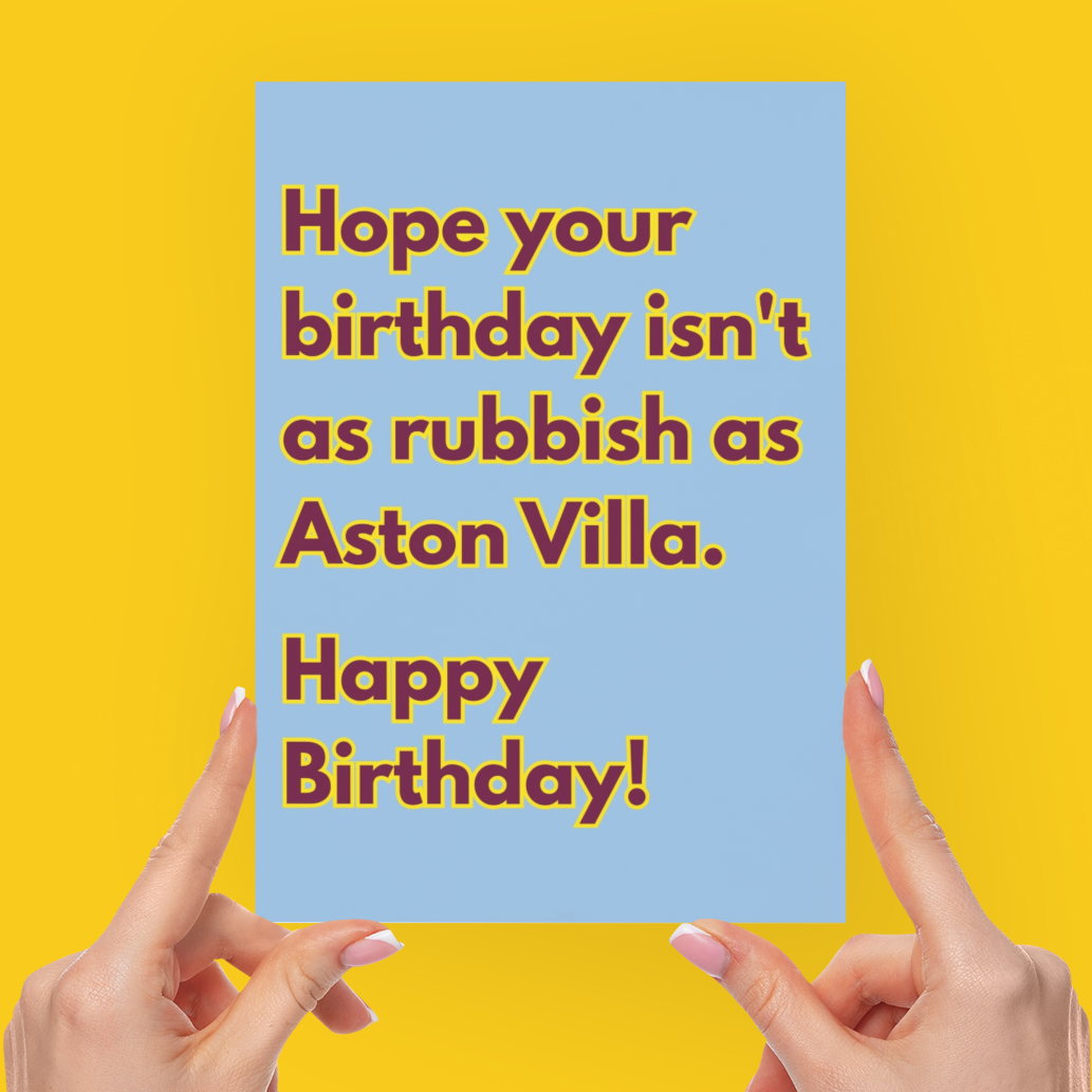 A person's hands holding a light blue greeting card with brown text that reads 'Hope your birthday isn't as rubbish as Aston Villa. Happy Birthday!' against a solid bright yellow background.