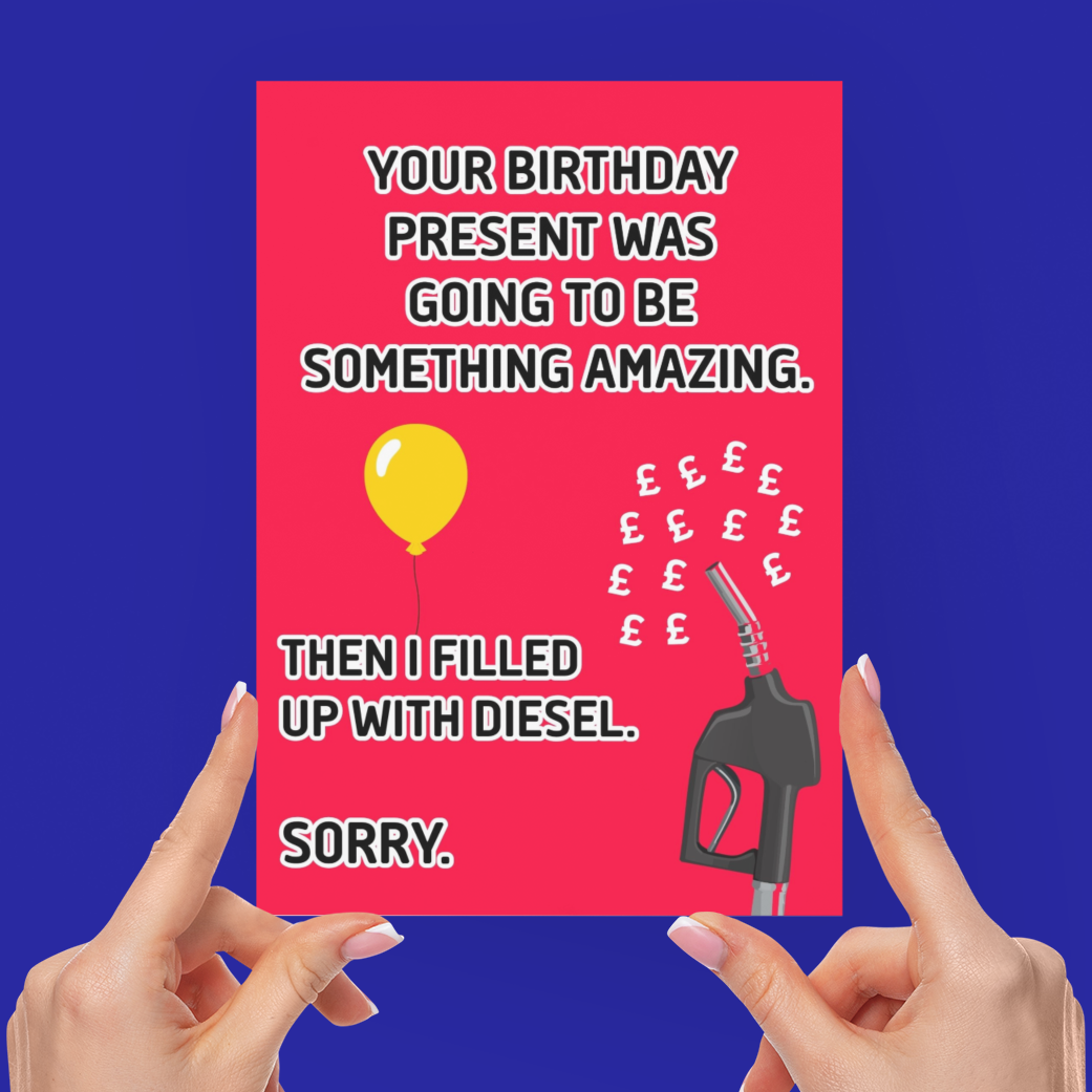 A person holds up a bright pink novelty greeting card with a humorous message about diesel and a balloon, with both hands visible against a solid blue background.