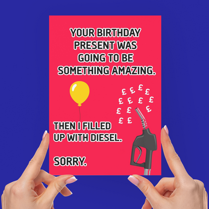 A person holds up a bright pink novelty greeting card with a humorous message about diesel and a balloon, with both hands visible against a solid blue background.
