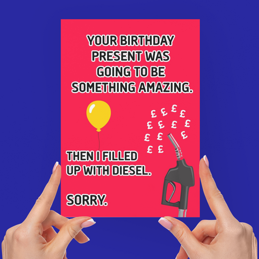 A person holds up a bright pink novelty greeting card with a humorous message about diesel and a balloon, with both hands visible against a solid blue background.