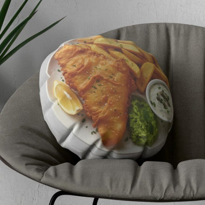 A round novelty pillow featuring a realistic print of a fish and chips meal, styled inside a gray peacock chair next to a potted plant.